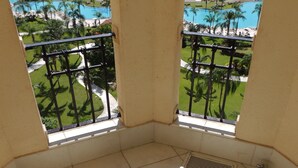 Une salle de bain d’angle avec une baignoire, deux fenêtres donnant sur une plage et des palmiers, et un balcon avec une balustrade.