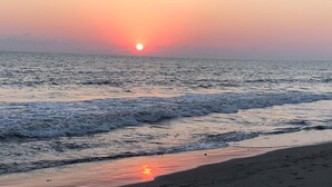 Un coucher de soleil sur une plage, avec des vagues qui viennent doucement lécher le rivage.