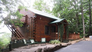 A rustic log cabin with a porch, outdoor seating, and a stone retaining wall. - Entire cabin for rent, 30-day minimum stay.   (Clayton)