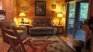 A cozy living room with a wooden interior, a sofa, a chair, a rug, and a fireplace. - Entire cabin for rent, 30-day minimum stay.   (Clayton)