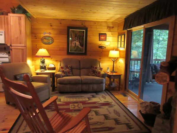 A cozy living room with a wooden interior, a sofa, a chair, a rug, and a fireplace. - Entire cabin for rent, 30-day minimum stay. (Clayton)