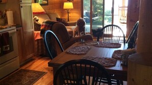 A cozy cabin interior with a wooden dining table, chairs, a sofa, and a dog. - Entire cabin for rent, 30-day minimum stay.   (Clayton)