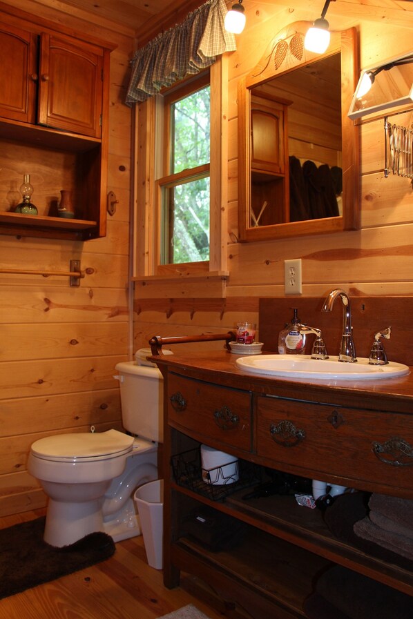 A wooden cabin bathroom with a white toilet, a wooden vanity with a sink, and a window above the mirror.