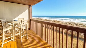 Une terrasse en bois avec une table et des chaises, donnant sur une plage avec des vagues et des dunes.