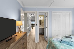 A hotel room with a TV, lamp, bed with blankets, and a hallway leading to a bathroom.