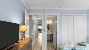 Une chambre d’hôtel équipée d’une télévision, d’une lampe, d’un lit avec des couvertures, et d’un couloir menant à une salle de bain.