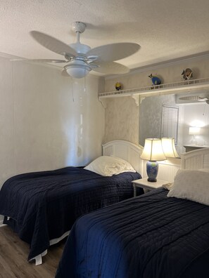 A hotel room with two beds, a ceiling fan, a nightstand with a lamp, and decorative items on the wall. - Great condo east of Shore Drive.  (Myrtle Beach)