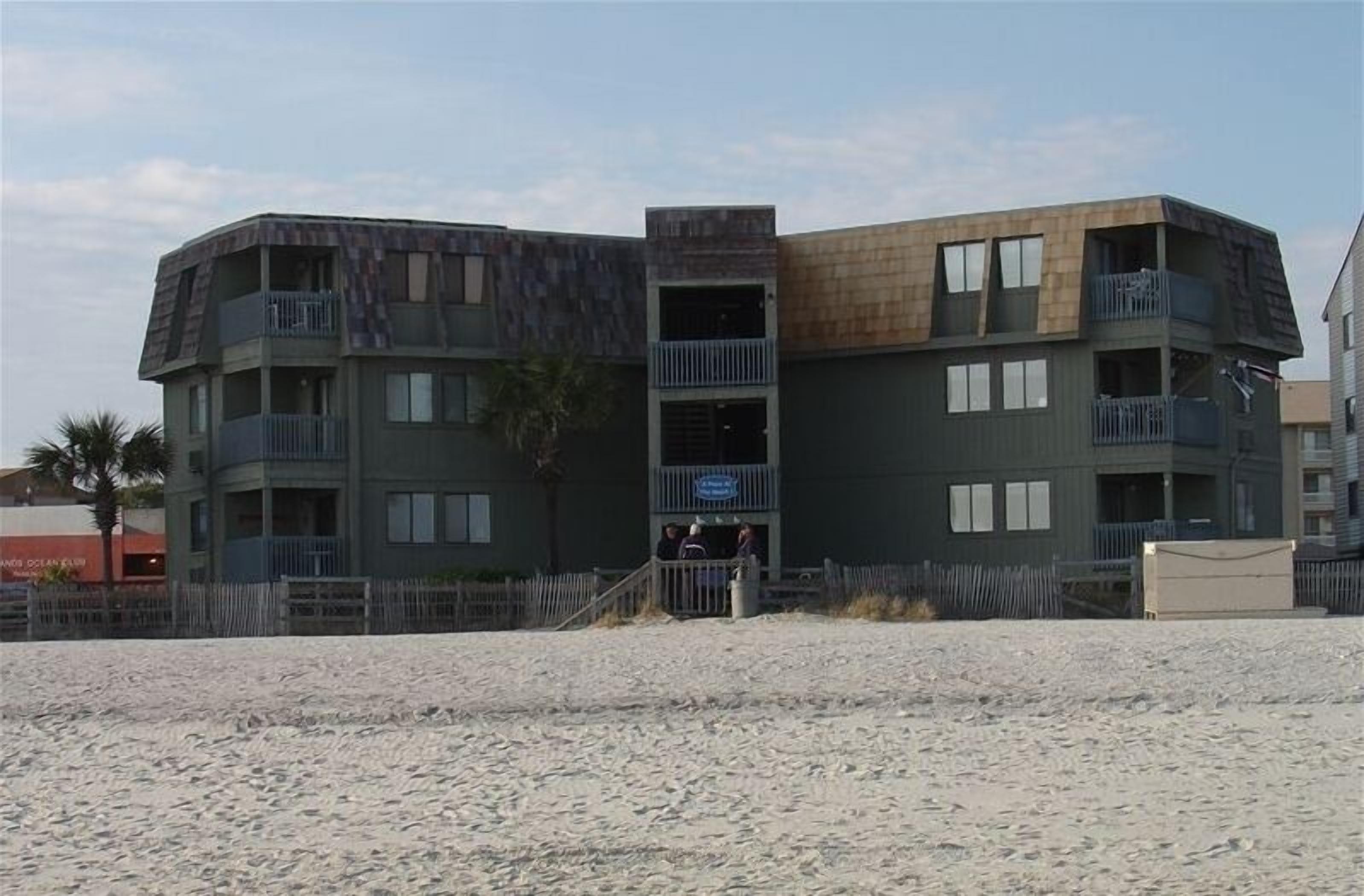 A multi-story building with balconies, located near a sandy area.