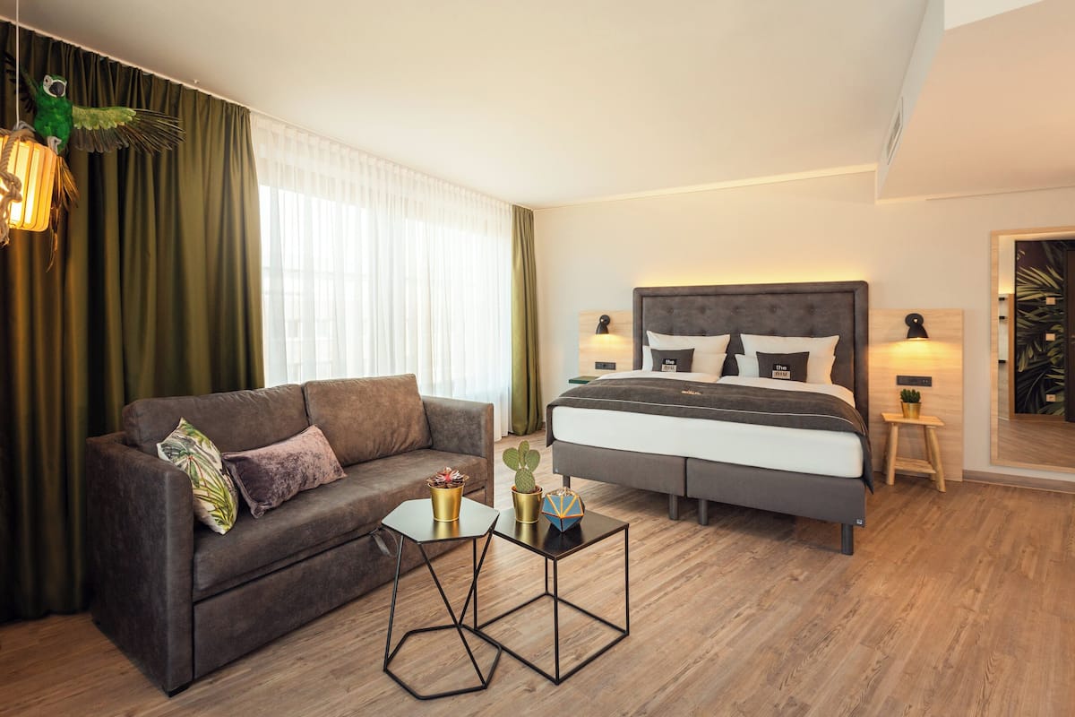 Een moderne hotelkamer met een bed, een bank, een salontafel en een klein bijzettafeltje.