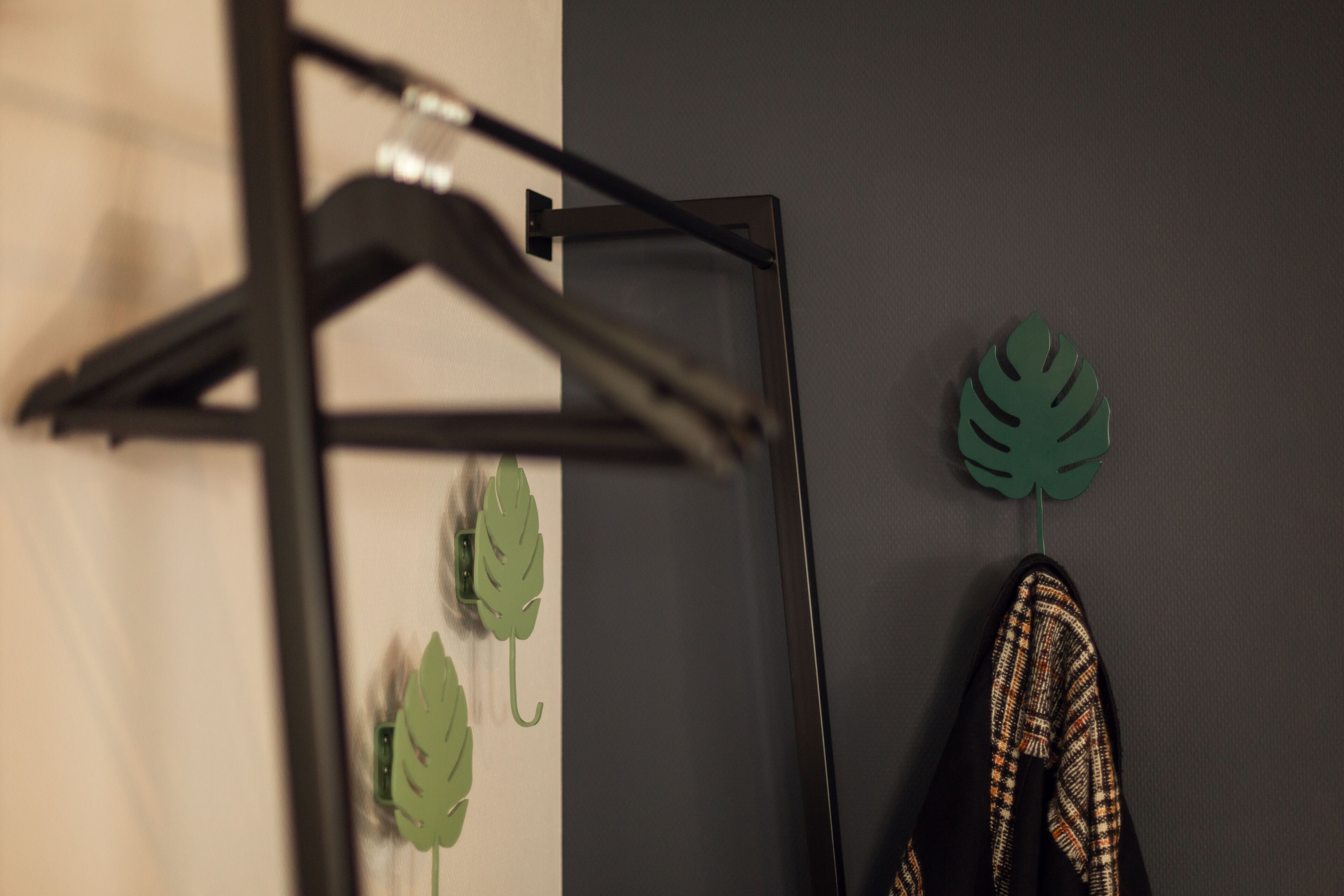 Een zwarte metalen kapstok met een groene bladdecoratie en een paar geruite schoenen voor een grijze muur.