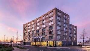 Un hotel moderno con fachada geométrica, varias ventanas y una entrada bien iluminada.