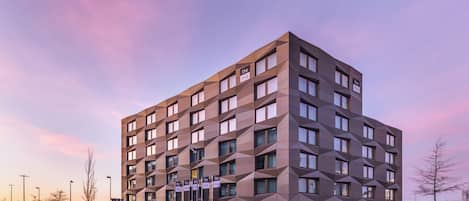 A modern hotel with a geometric facade, multiple windows, and a well-lit entrance.