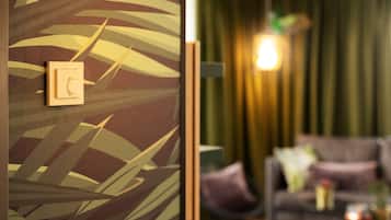 Habitación con un panel decorado con motivos de hojas y un tablero eléctrico de madera. Se observa un sofá y una lámpara al fondo.