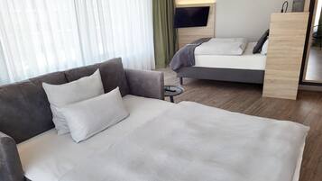 Habitación de hotel con una cama grande, un sofá, un televisor montado en la pared y suelo de madera.