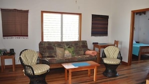 A living room with a sofa, two armchairs, a small wooden table, and a window with blinds. - Beach Front Rental, Casita Del Mar, Hopkins, Belize (Hopkins)