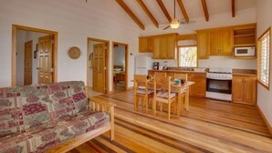 A spacious living area with a wooden floor, a sofa, a dining table with chairs, and a kitchen with wooden cabinets and appliances. - Beach Front Rental, Casita Del Mar, Hopkins, Belize (Hopkins)
