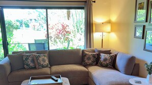 Ein Wohnzimmer mit Ecksofa, einem Pouf, einem Beistelltisch und einem Deckenventilator.