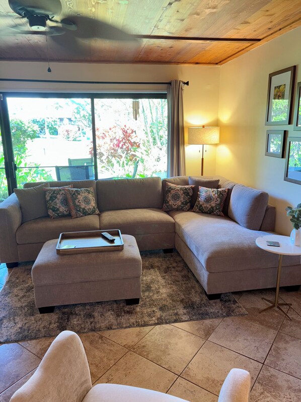A living room with a sectional sofa, a small ottoman, a side table, and a ceiling fan.