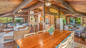A spacious wooden dining area with a long table and chairs, a ceiling fan, and a kitchen in the background.