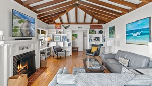 Ein geräumiges Wohnzimmer mit Kamin, Holzbalken und Kunstwerken an den Wänden.