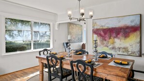 Ein Esszimmer mit Holztisch, schwarzen Stühlen, einer Chandelierleuchtre und Kunstwerken an den Wänden.