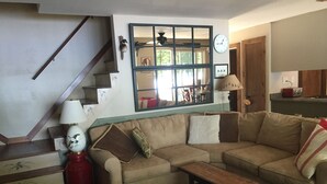 A living room with a sofa, a coffee table, a lamp, a clock, and a staircase. - Camp Pinecone--Waterfront Home on Upper Saranac Lake (Saranac Lake)