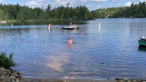 A lake with a dock, a sandy shore, and a forest in the background. - Camp Pinecone--Waterfront Home on Upper Saranac Lake (Saranac Lake)