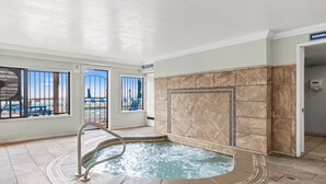Wellnessbereich mit Whirlpool, gefliestem Boden und Blick auf einen Strand durch große Fenster.