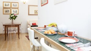 A dining area with a long table set for breakfast, including croissants, fruit, and a cup. There are chairs, a vase with flowers, and framed pictures on the wall. - Beautiful, Bright, Spacious in Historic Bologna, great atmosphere, renovated (Bologna)