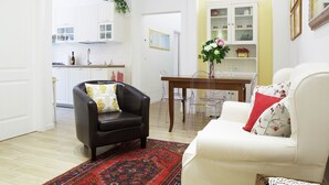 A living room with a black leather armchair, a white sofa, a dining table with chairs, and a kitchen in the background. - Beautiful, Bright, Spacious in Historic Bologna, great atmosphere, renovated (Bologna)