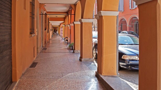 A corridor with arches and a tiled floor, leading to a building with a red facade. - Beautiful, Bright, Spacious in Historic Bologna, great atmosphere, renovated (Bologna)