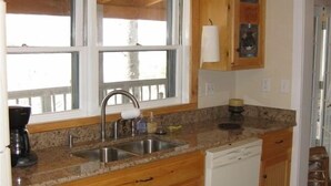 A compact kitchen with wooden cabinets, a built-in dishwasher, and a window above the sink. - Charming Bear Paw Cabin with Spectacular View of Lake Hiwassee (Murphy)