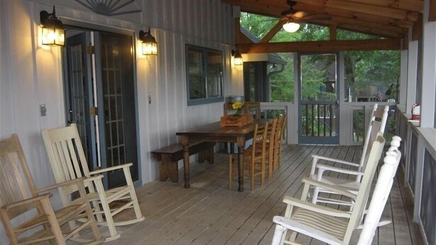 A covered porch with wooden furniture, including a table and chairs, and a view of the outdoors. - Charming Bear Paw Cabin with Spectacular View of Lake Hiwassee (Murphy)