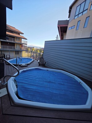 A rooftop with two above-ground swimming pools, a wooden deck, and a view of surrounding buildings.