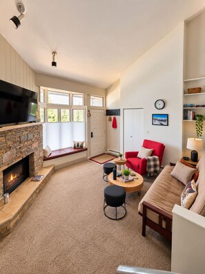 A living room with a fireplace, a red sofa, a beige sofa, a coffee table, and a television. - 300 steps to the slopes, Cozy Split-Level Loft, Fireplace, Hot Tubs, Free Bus (Steamboat Springs)