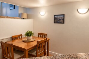 A dining area with a wooden table, four chairs, a potted plant, and wall-mounted lighting.