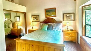 Een slaapkamer met een houten bed, twee nachtkastjes met lampen, een groot raam en kunstwerken aan de muur.