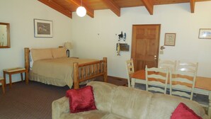 Een gezellige kamer met een bed, een houten hoofdbord, een bank met rode kussens, een houten tafel en een stoel.