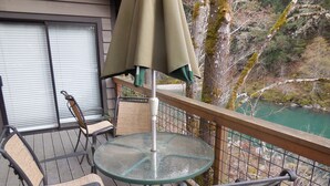 Een terras met een glazen tafel en stoelen, met uitzicht op een rivier.
