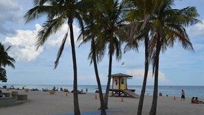 Ein Strand mit Palmen, einem Rettungsturm und entspannten Menschen.