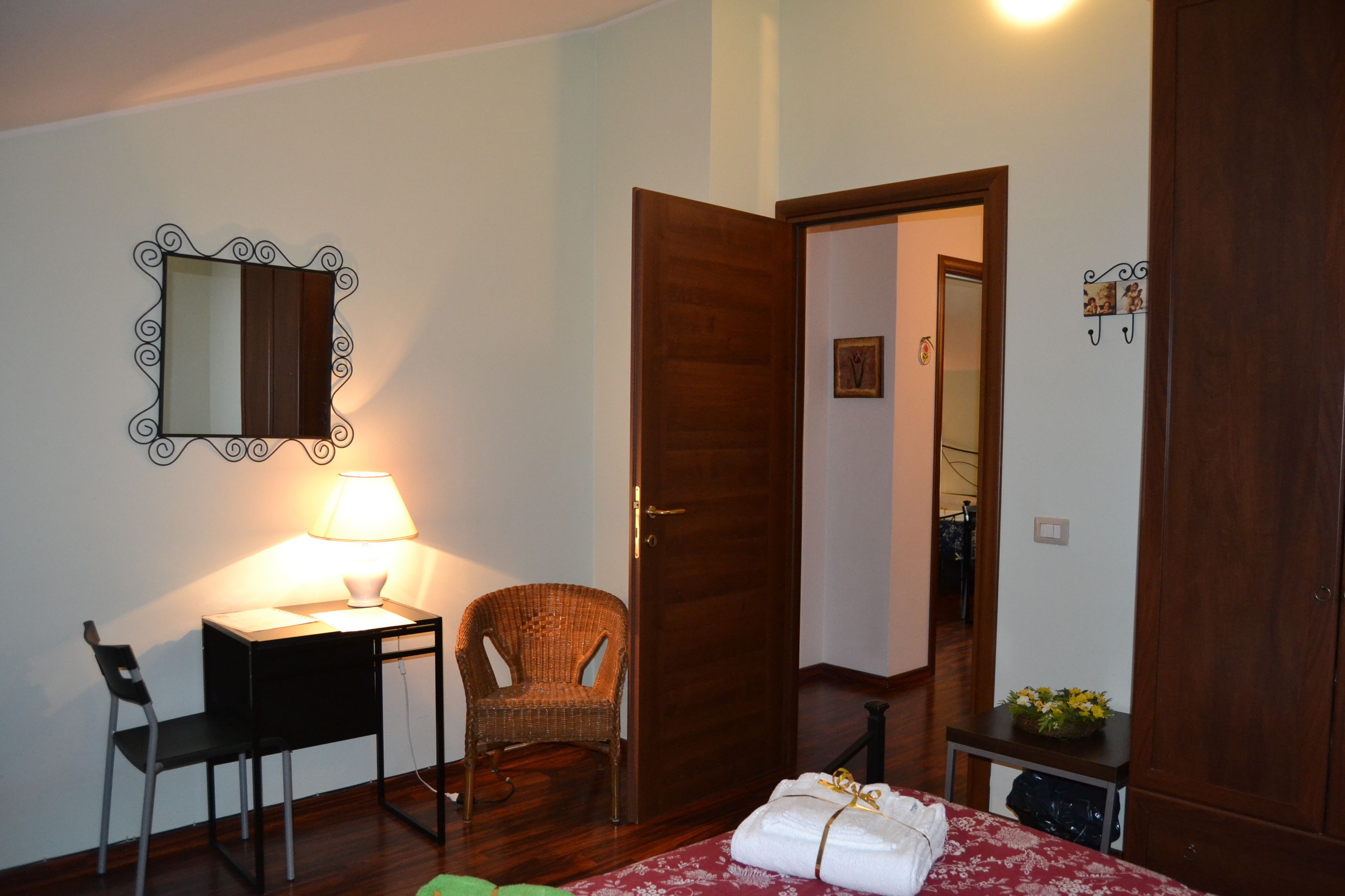 A bedroom with a bed, a desk with a lamp, a chair, a wardrobe, and a mirror on the wall.