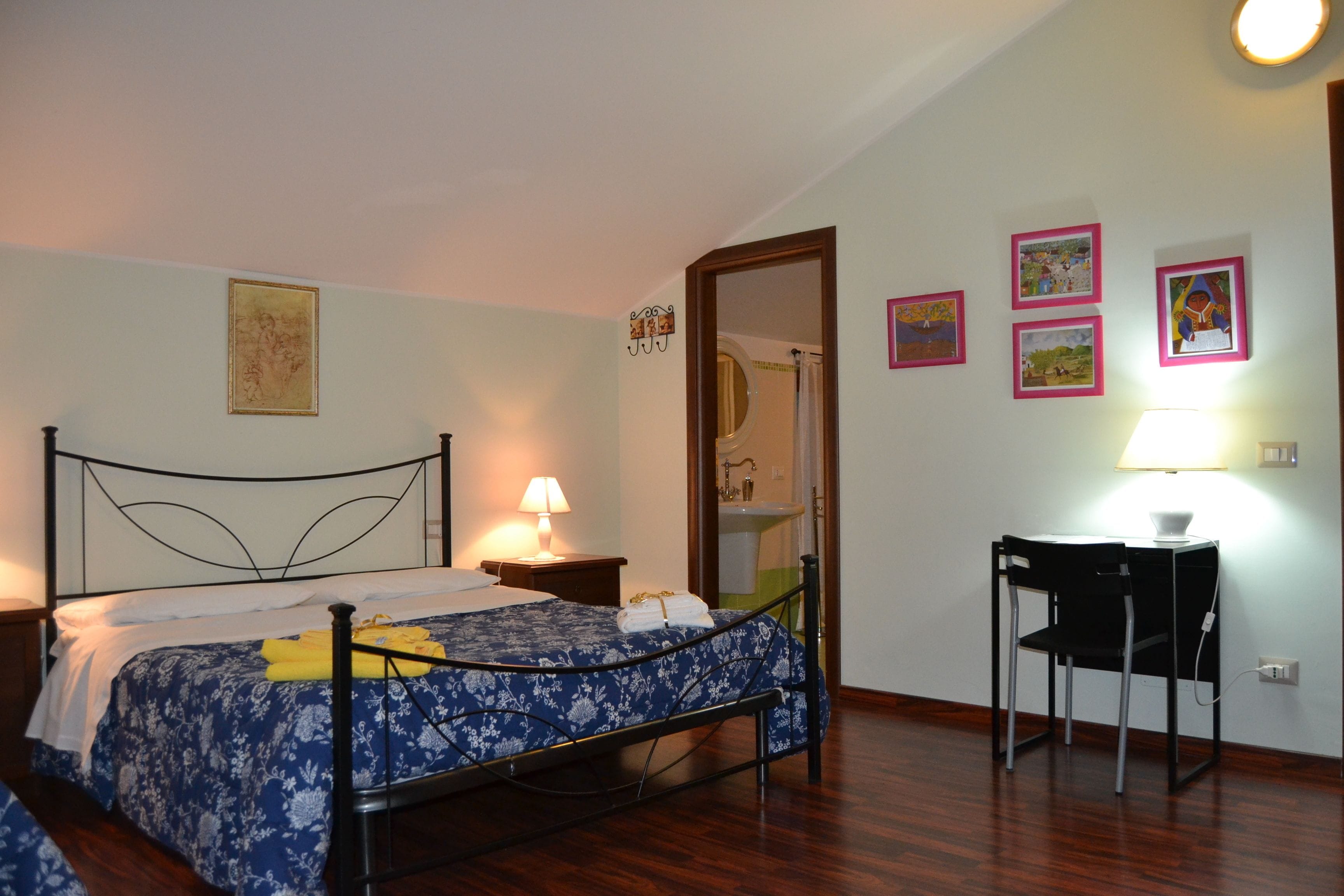 Ein Schlafzimmer mit Bett, Nachttisch, Sessel und Wandbildern.