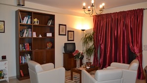 A living room with a bookshelf, two white armchairs, a coffee table, a television, and a red curtain. - B&B Il Mulino (Guardiagrele)