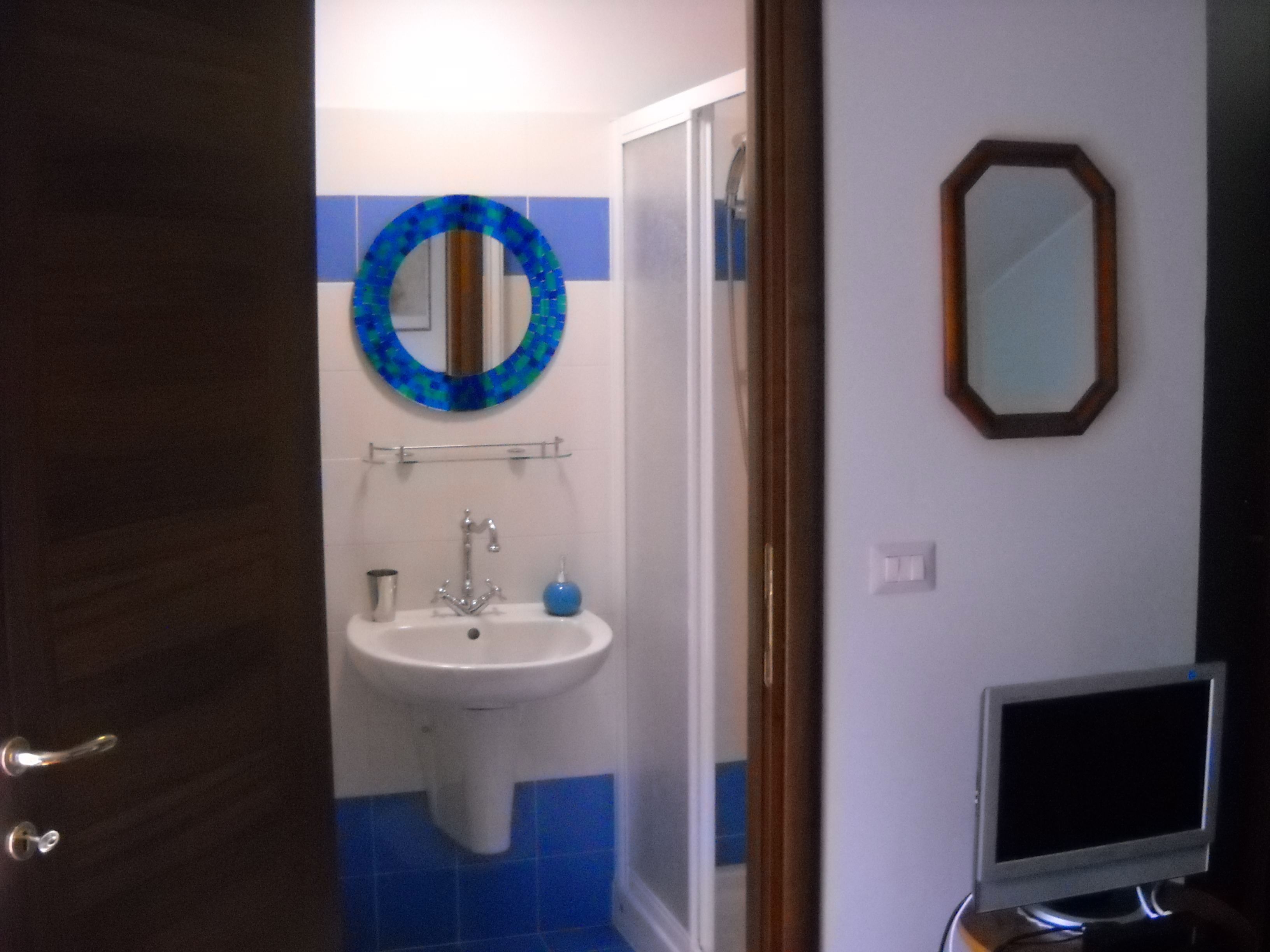 A bathroom with a sink, mirror, and a television on a stand.