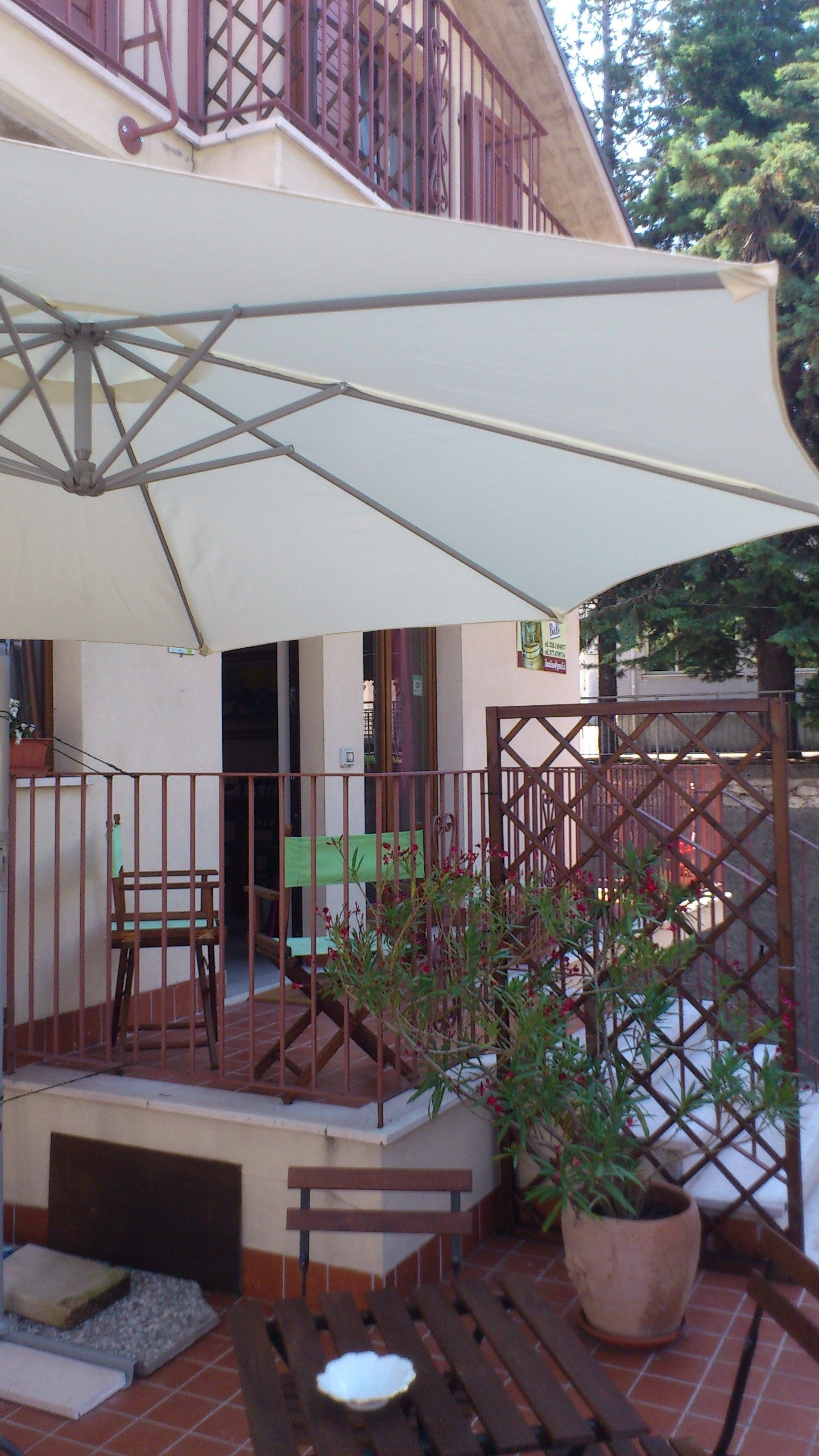 A covered outdoor seating area with a table and chairs, a potted plant, and a staircase leading to an upper level.