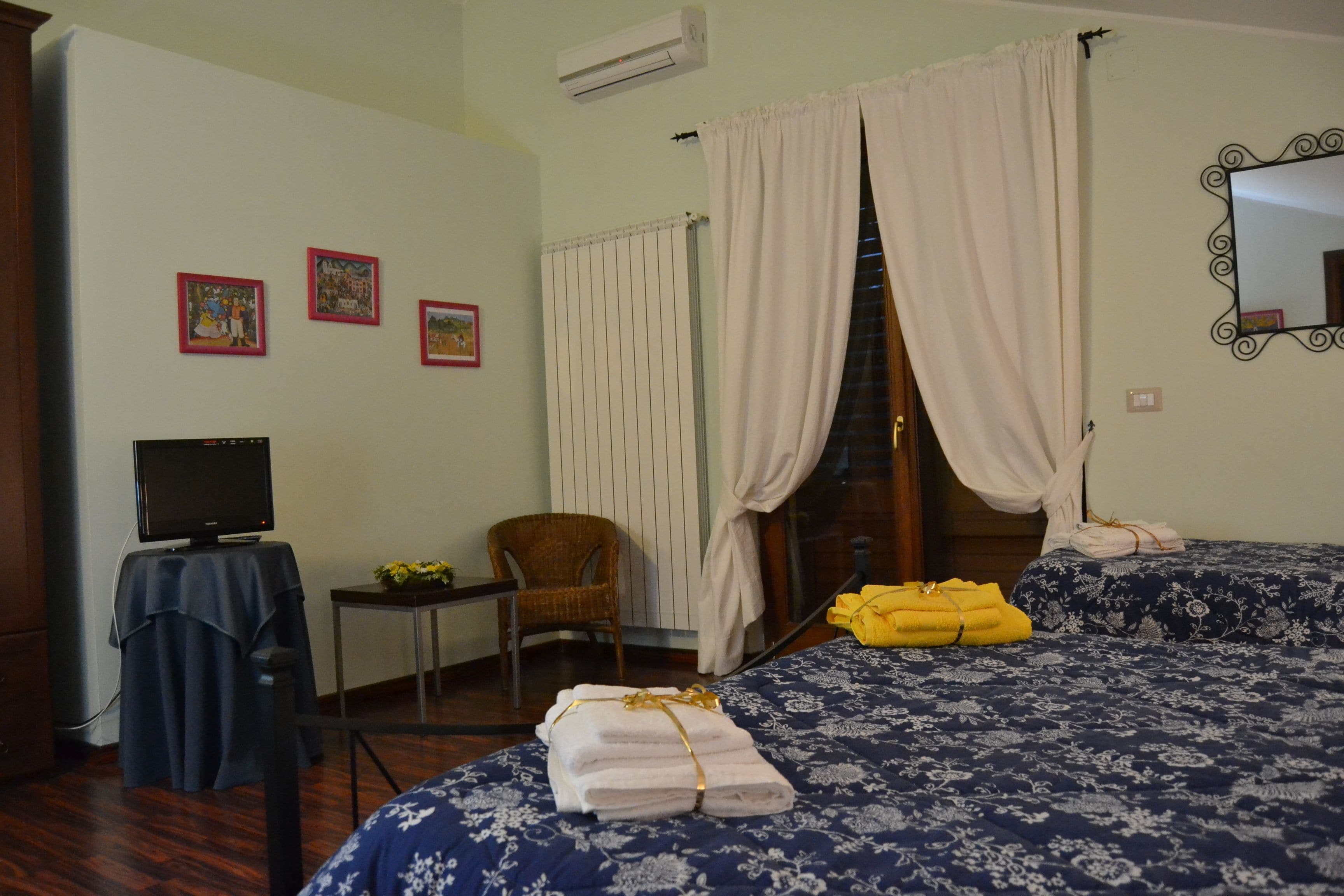 A hotel room with a bed, a chair, a table with a TV, and a window with curtains.