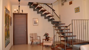 A staircase with wooden steps and metal railings, a wooden door, two armchairs, a small table with a vase, and a chandelier. - B&B Il Mulino (Guardiagrele)