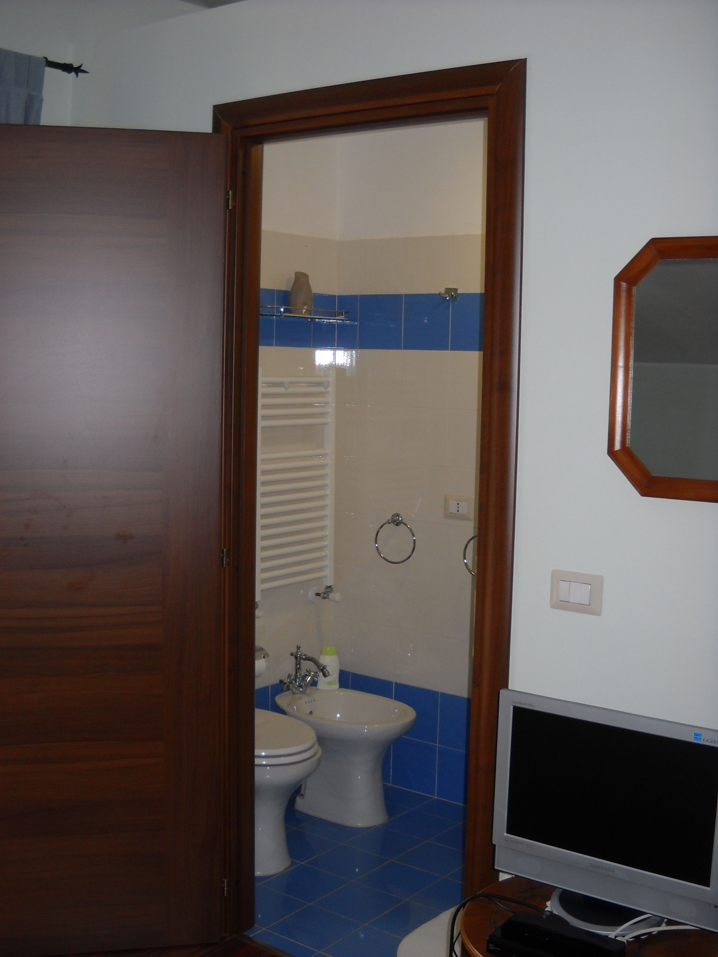 Uma casa de banho com porta de madeira, sanita, bidé e espelho na parede.