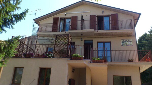 A two-story building with a balcony on the upper floor, a small entrance on the ground floor, and a sign advertising a local business. - B&B Il Mulino (Guardiagrele)