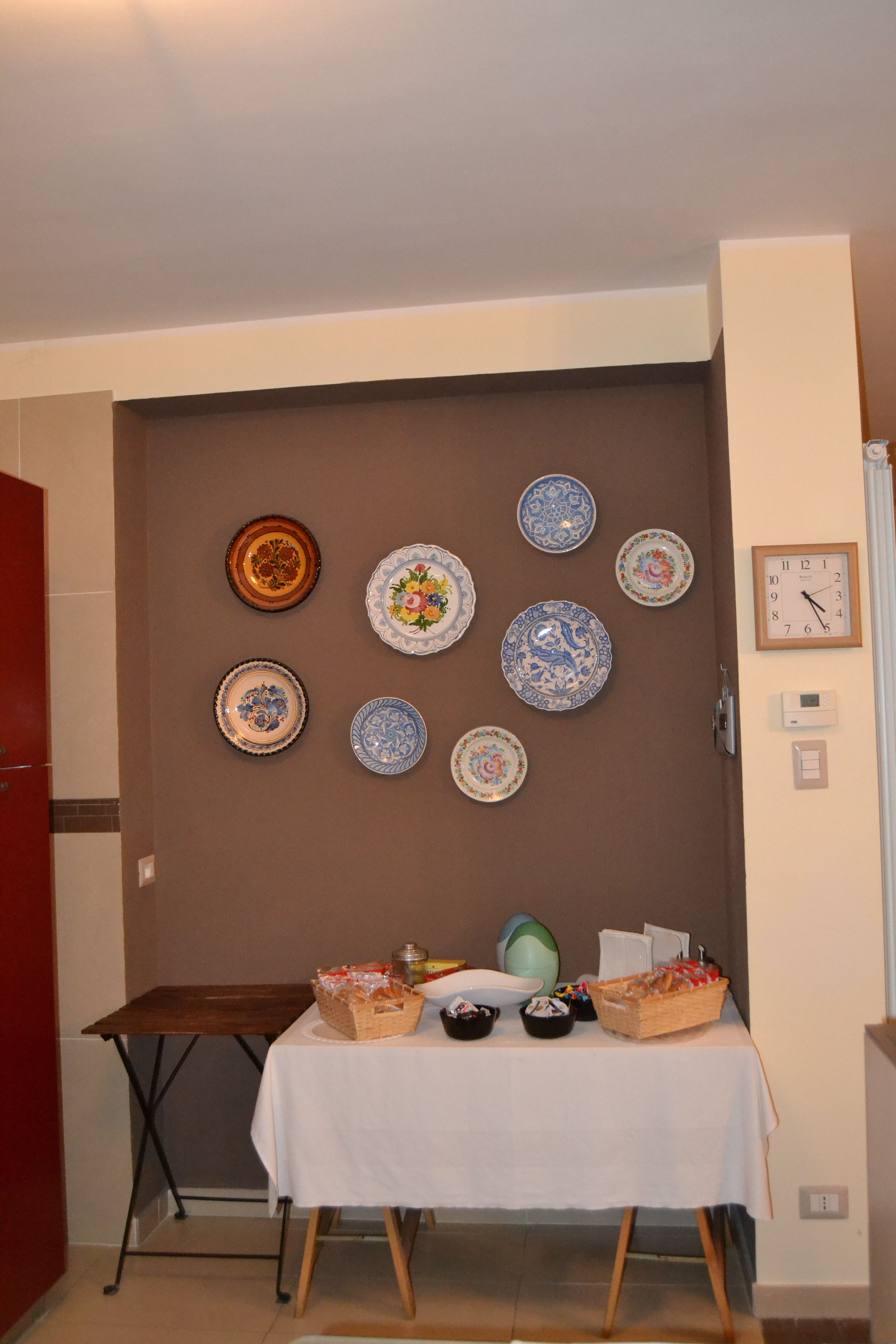 A room with a wall decorated with various plates and a table with baskets and bowls.